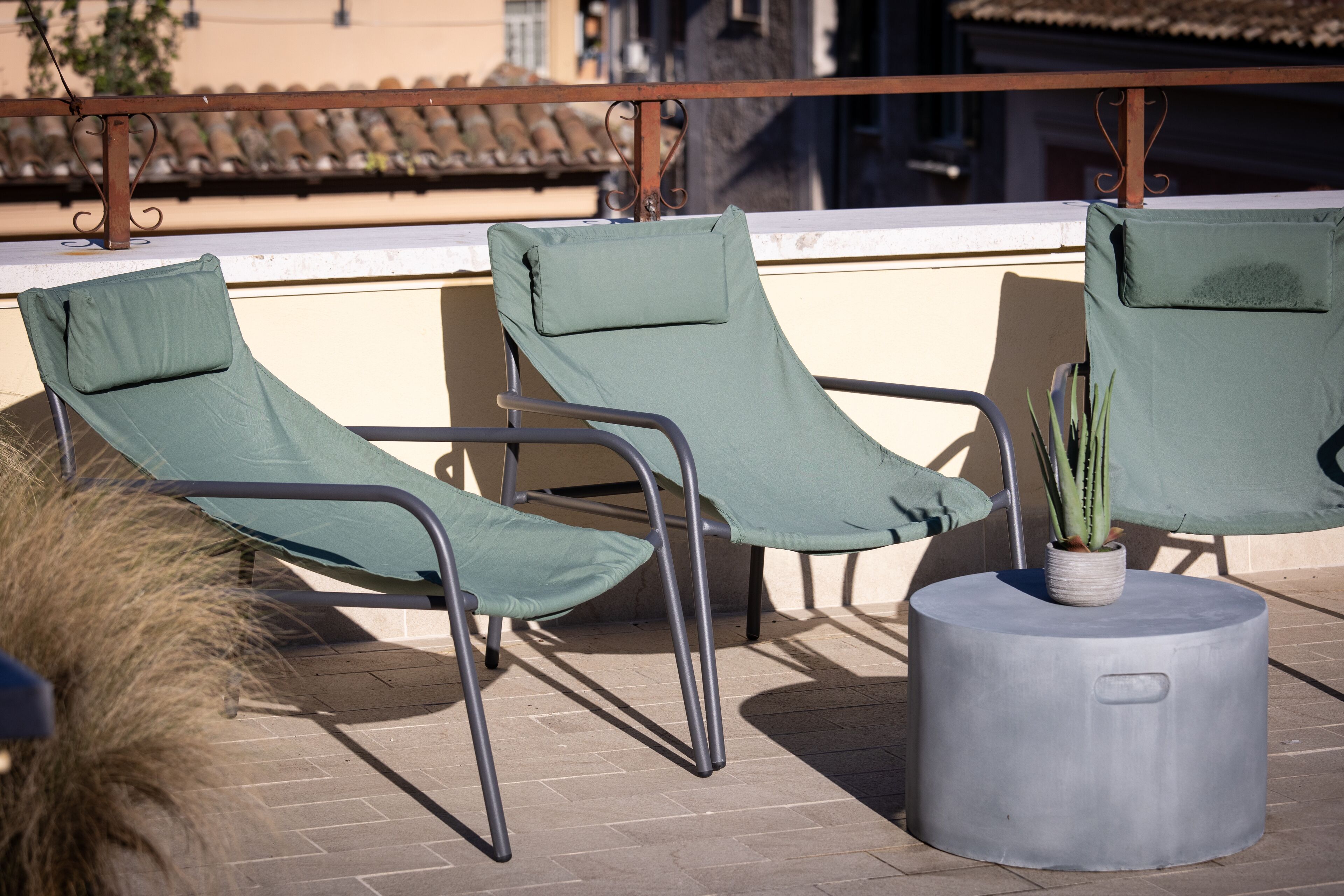 Een terras op het dak met drie groene loungestoelen en een ronde tafel met een potplant.