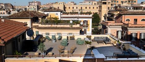 A rooftop terrace with outdoor seating, a view of the city, and a building with a tiled roof.