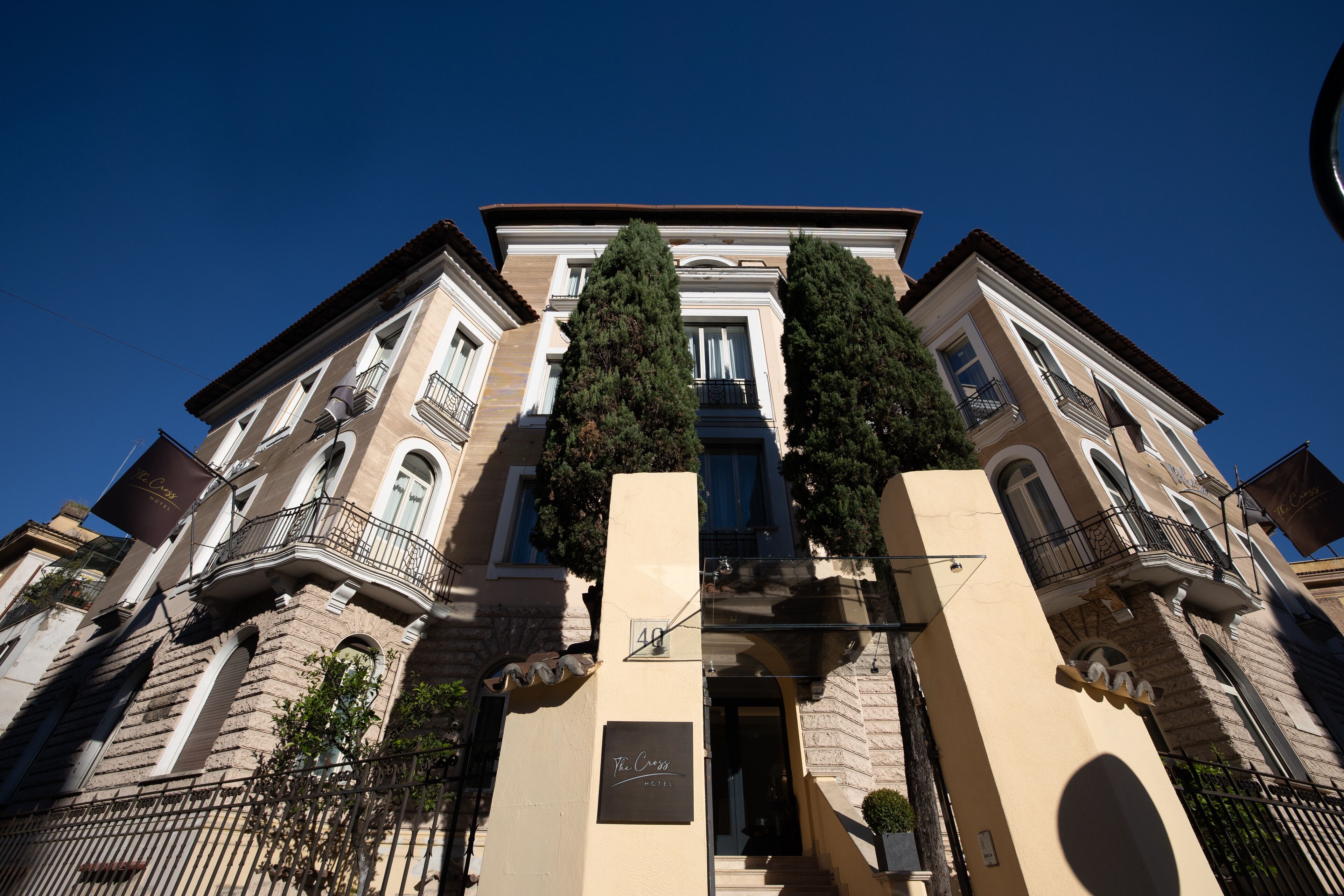 A hotel facade with a central entrance, two tall trees, and a clear blue sky.