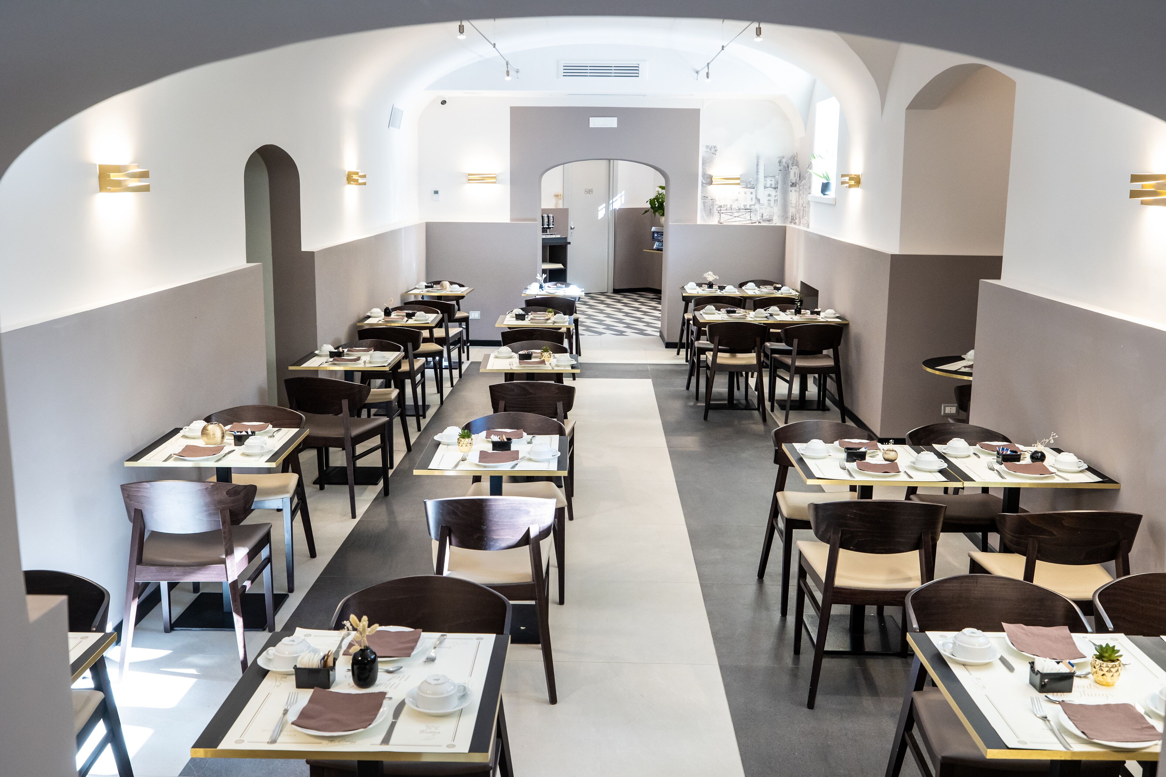 A modern restaurant with a central aisle, tables set with white tablecloths, and dark wooden chairs.
