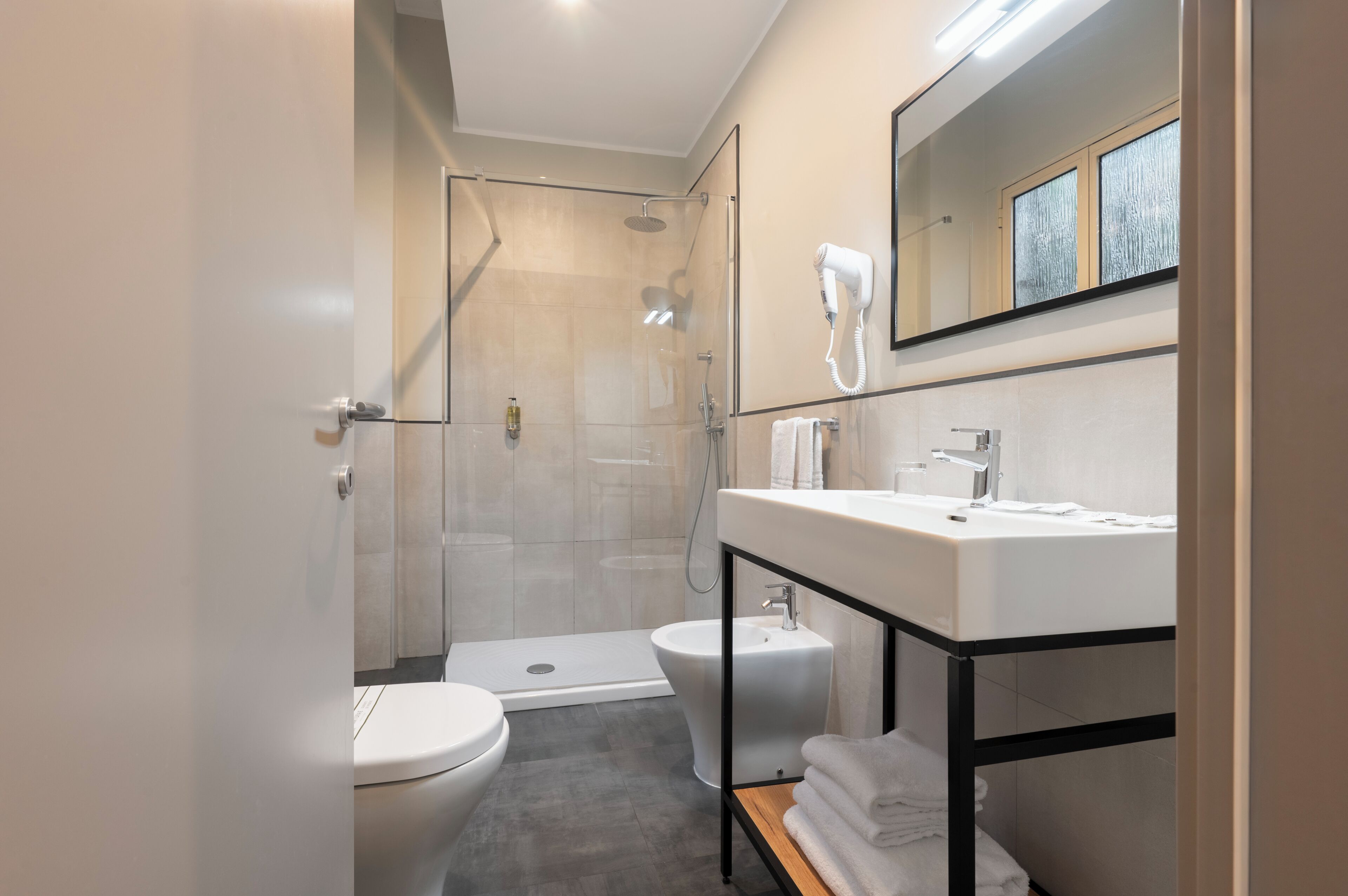 A modern bathroom with a toilet, bidet, shower, and a vanity with a mirror.