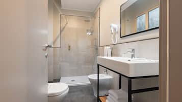 A modern bathroom with a toilet, bidet, shower, and a vanity with a mirror.