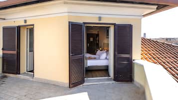 Un apartamento pequeño de un dormitorio con balcón, que incluye una cama, una mesita y una ventana con contraventanas.