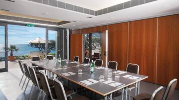 A conference room with a long table, chairs, and a view of the sea through large windows.