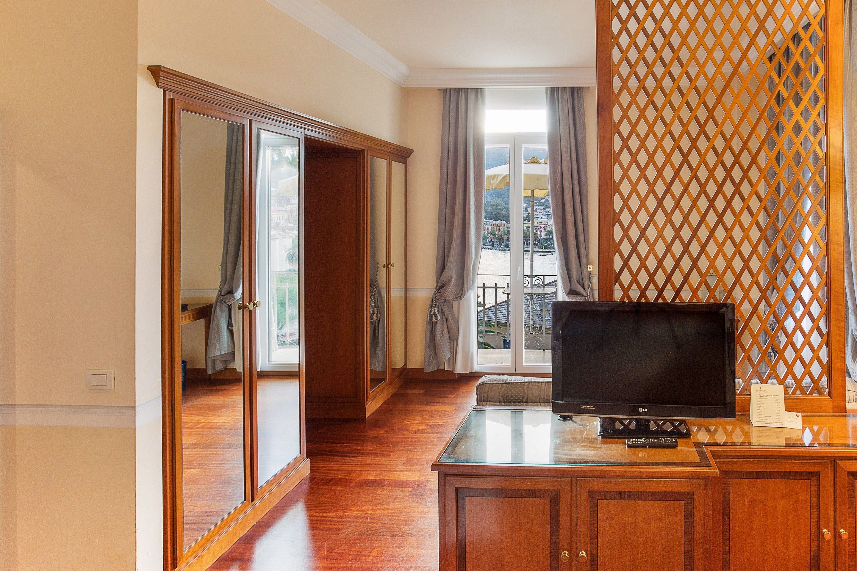 Una stanza con un armadio in legno, una televisione e vista su un balcone con ringhiera.