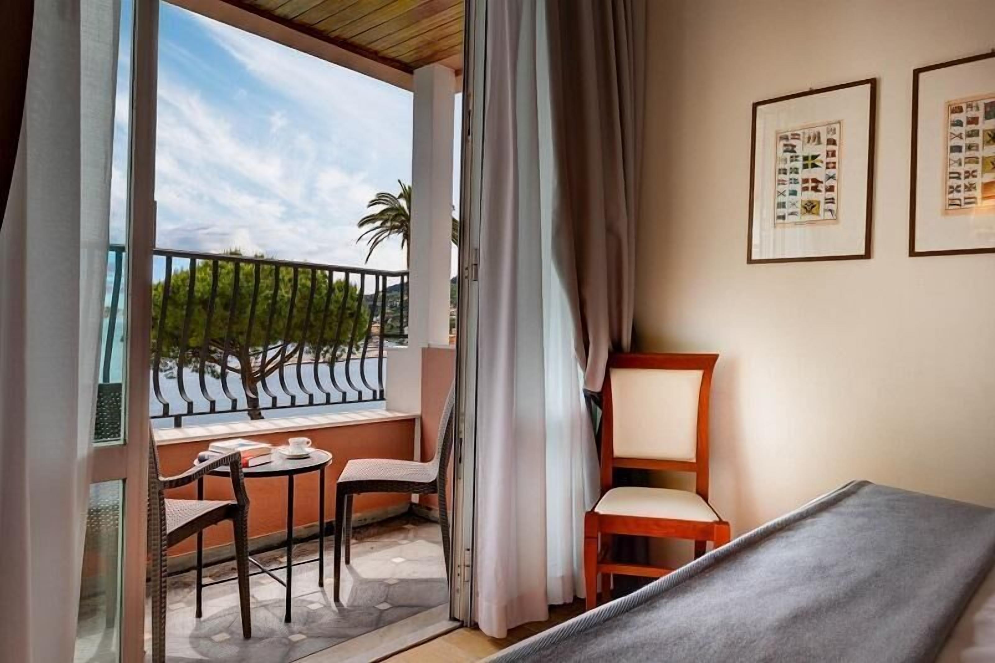 A room with a balcony, a bed, a chair, and a table.