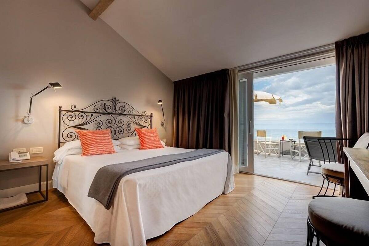 Een hotelkamer met een bed, nachtlampjes, een bureau en uitzicht op het balkon.