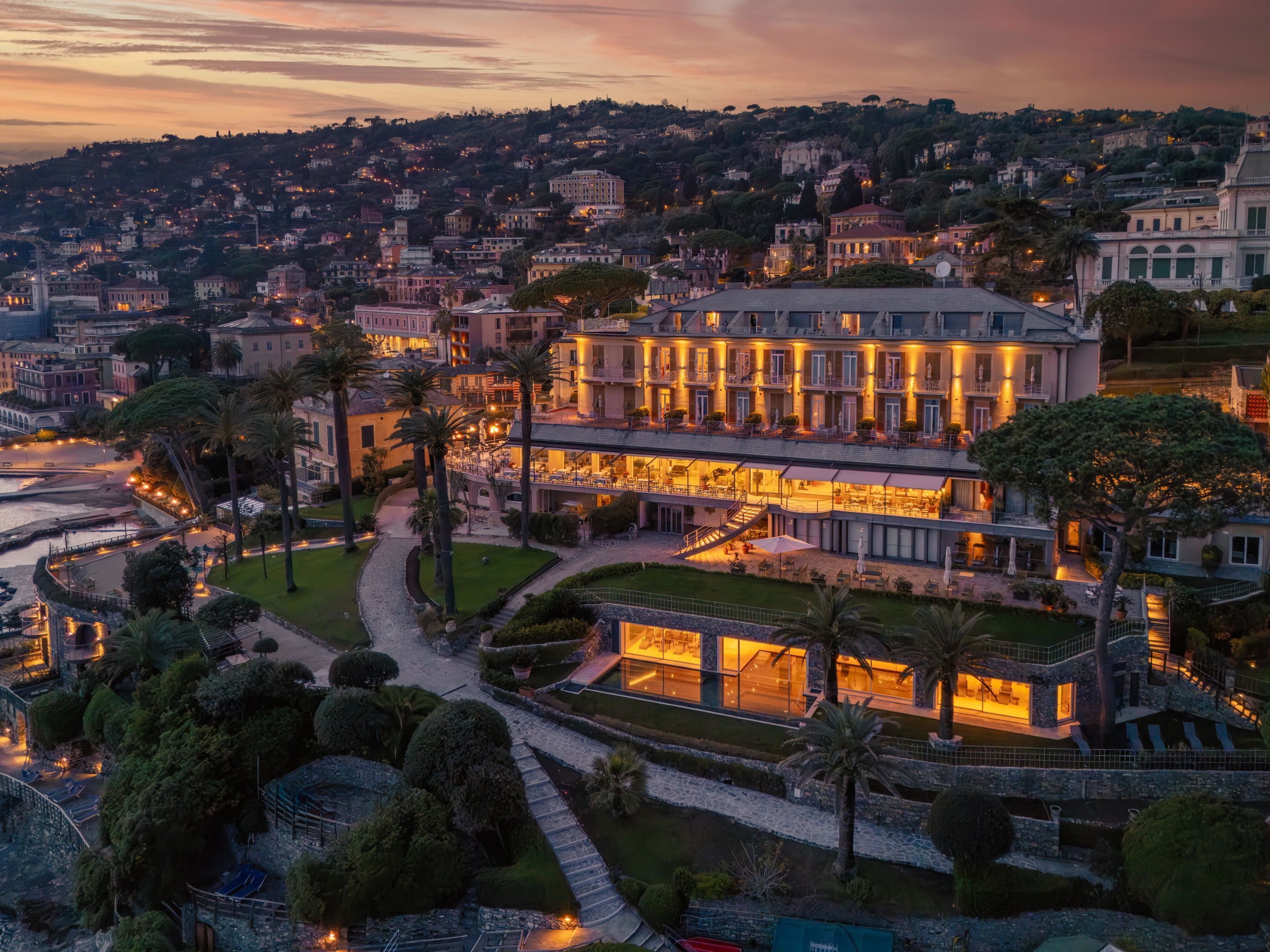 Un hotel grande de varios pisos con un jardín cuidado y vistas de la ciudad circundante.