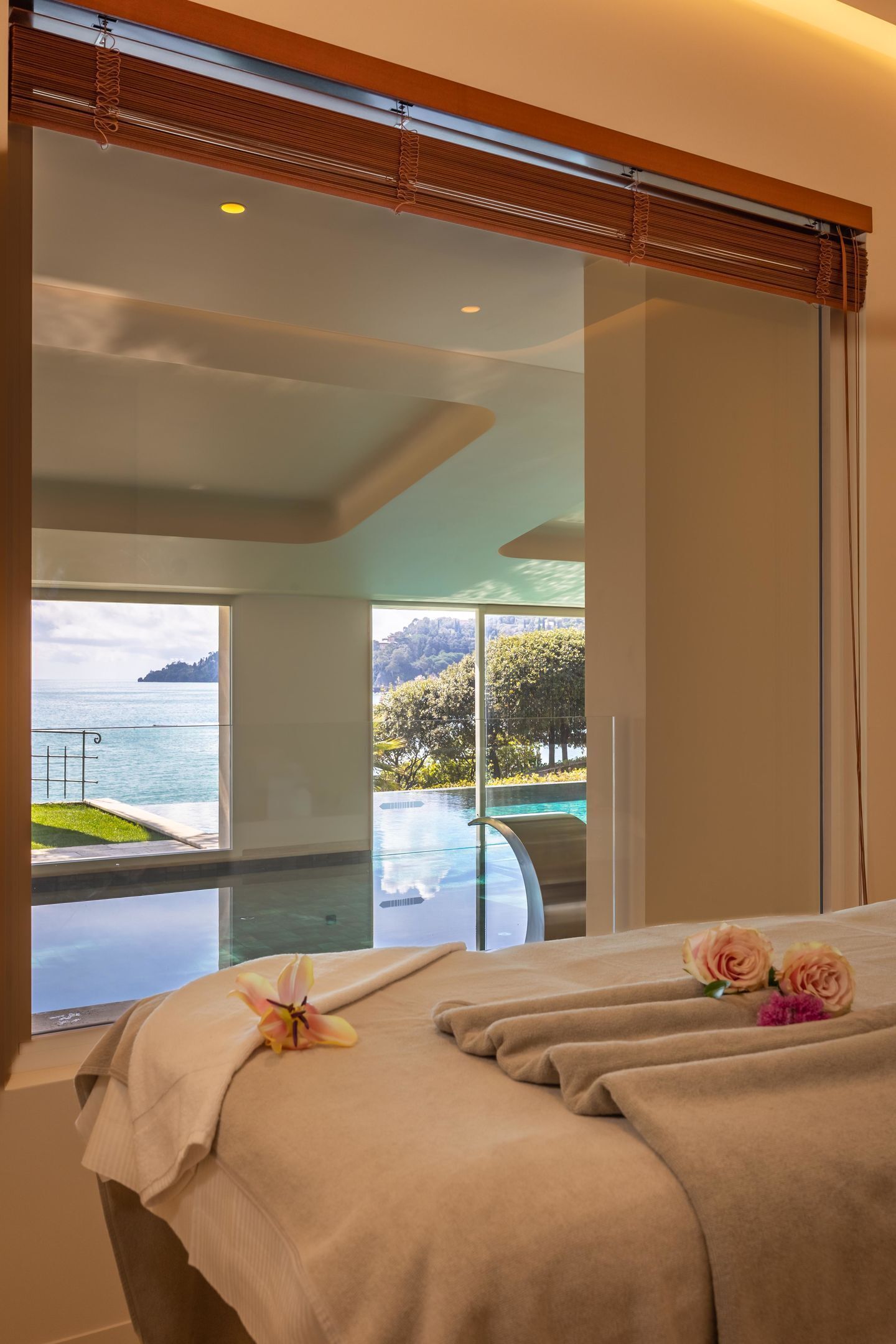 A hotel room with a large window offering a view of a pool and a distant island.