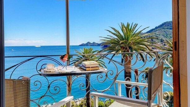Een balkon met uitzicht op zee, een tafel met een stoel en een gele parasol.