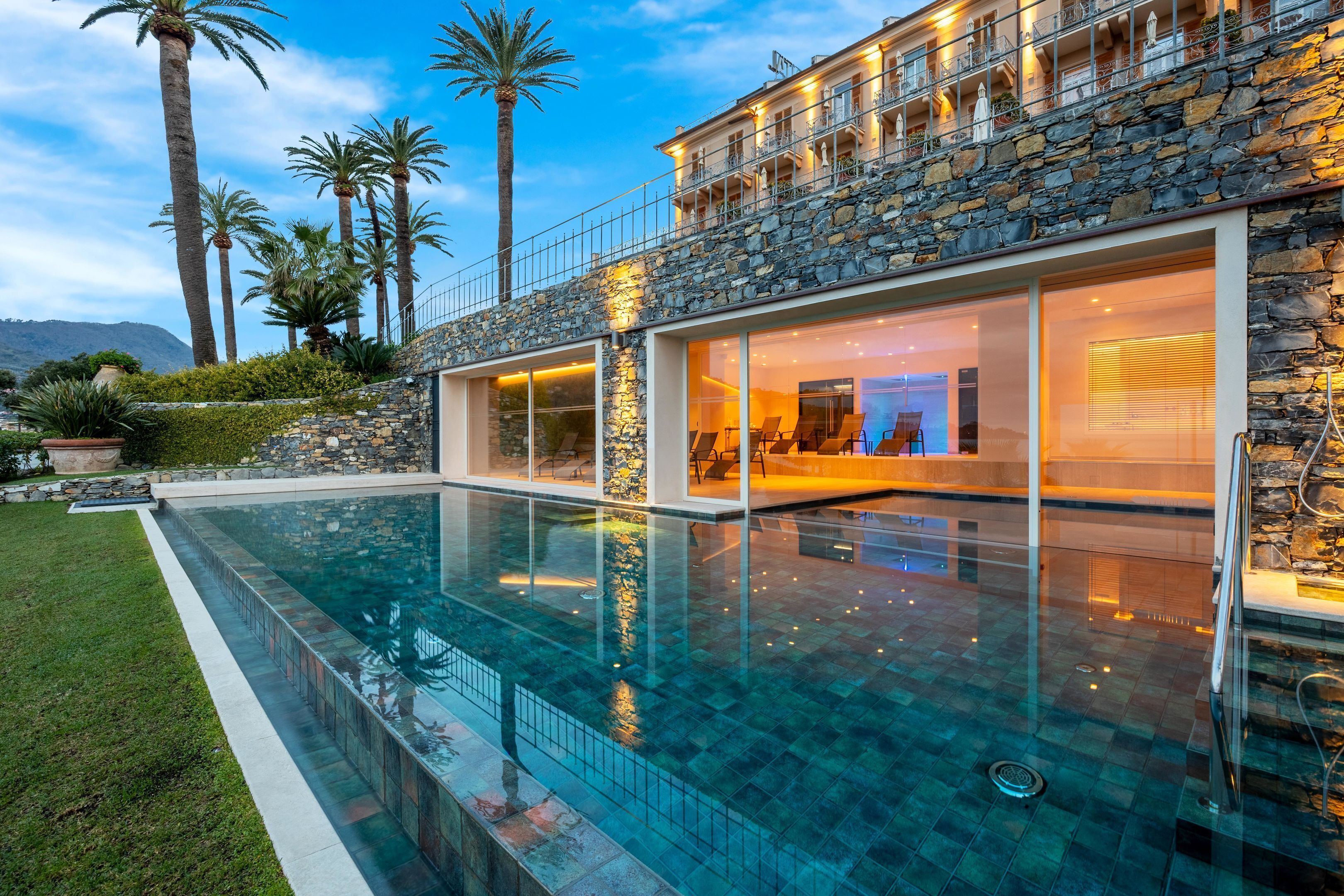 Una casa moderna con una amplia piscina, fachada de piedra y un balcón con vistas a la piscina.