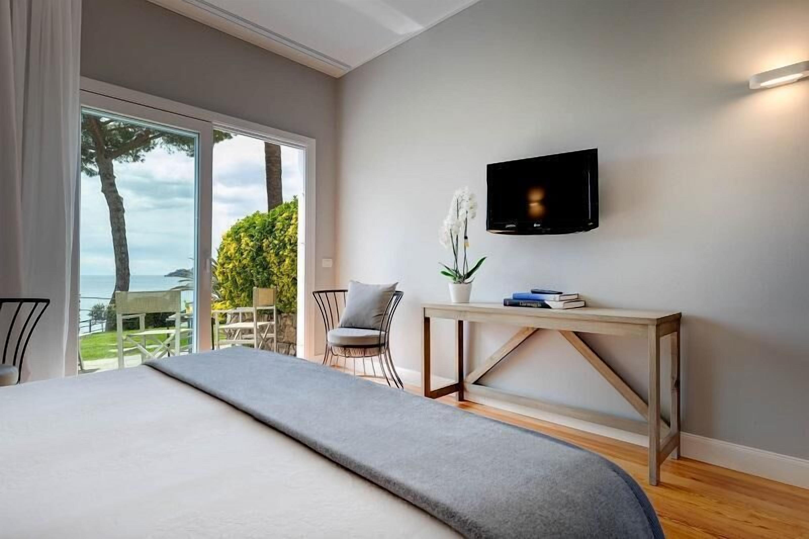 Un dormitorio con una cama grande, un televisor instalado en la pared, una mesita con una planta y vistas al exterior.