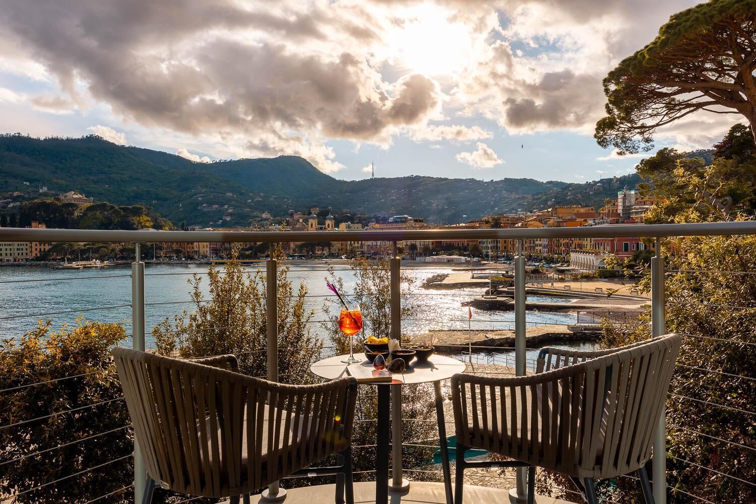 Una terraza con dos sillas de madera y una mesa, con vista a un río, un paisaje urbano y montañas al fondo.