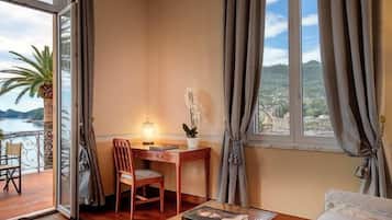 A room with a wooden desk, chair, and a view of the sea through a large window.
