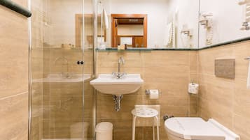 A bathroom with a glass-enclosed shower, a sink, a toilet, and a small stool.