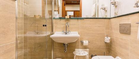 A bathroom with a glass-enclosed shower, a sink, a toilet, and a small stool.