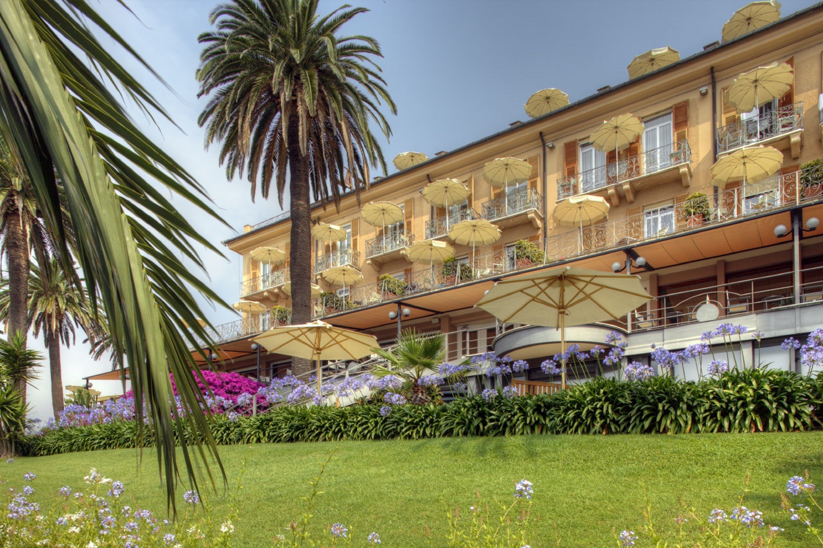 A hotel with multiple balconies, outdoor umbrellas, and lush garden landscaping.