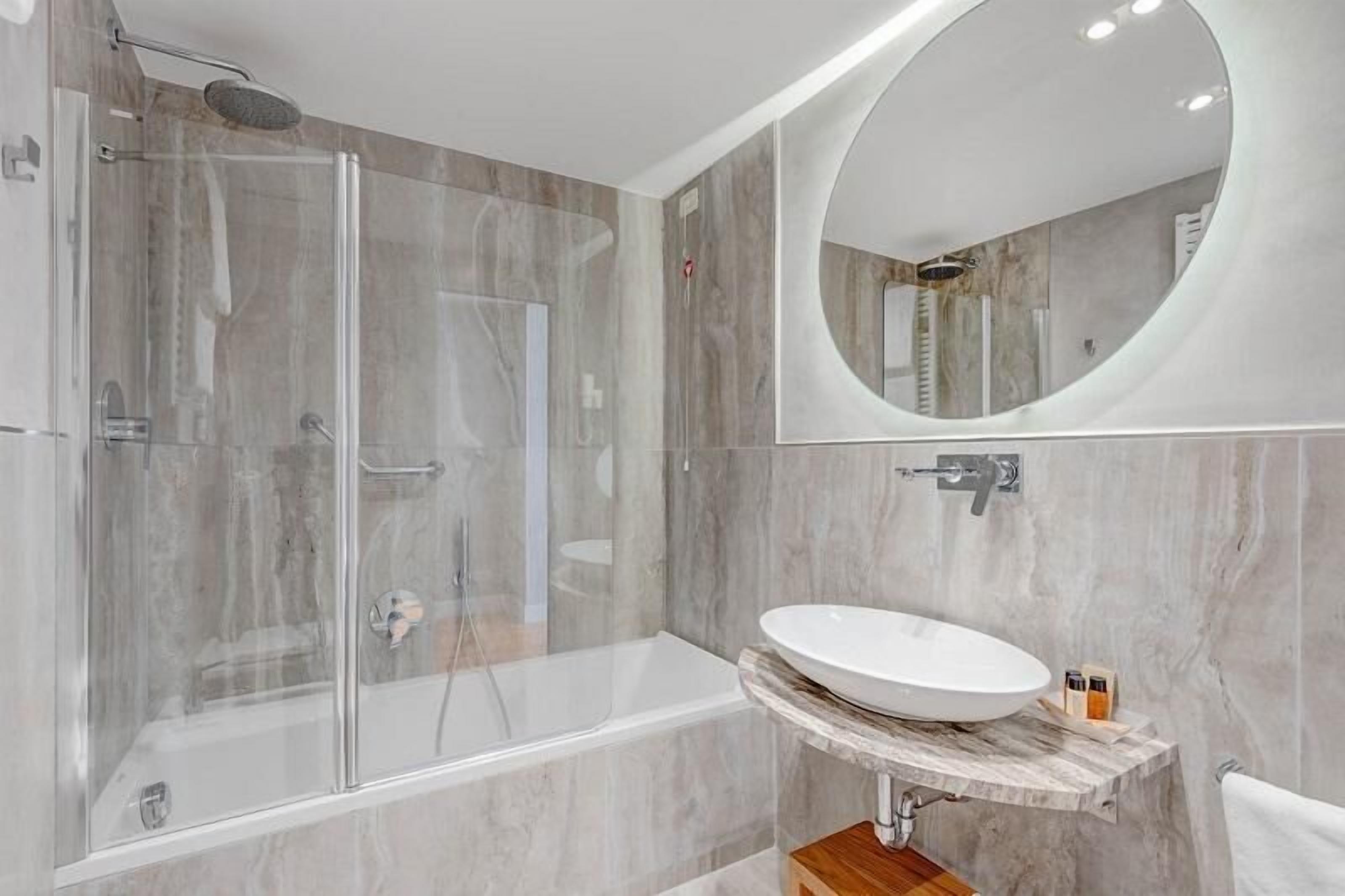 Een moderne badkamer met een douchecabine van glas, een vrijstaand bad en een marmeren wastafelmeubel met een wastafel.