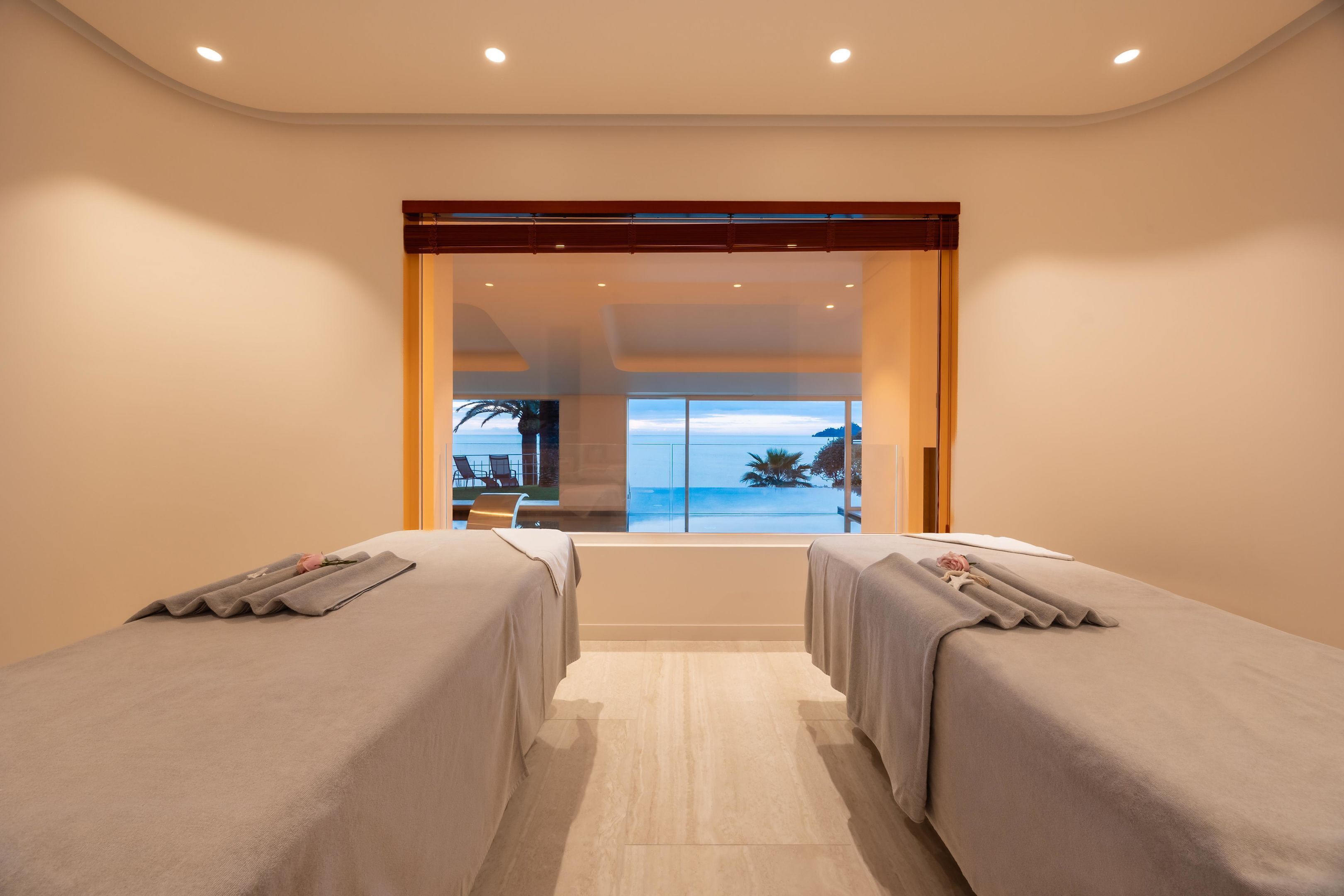A room with two beds, a view of the sea, and a door leading to an outdoor area.