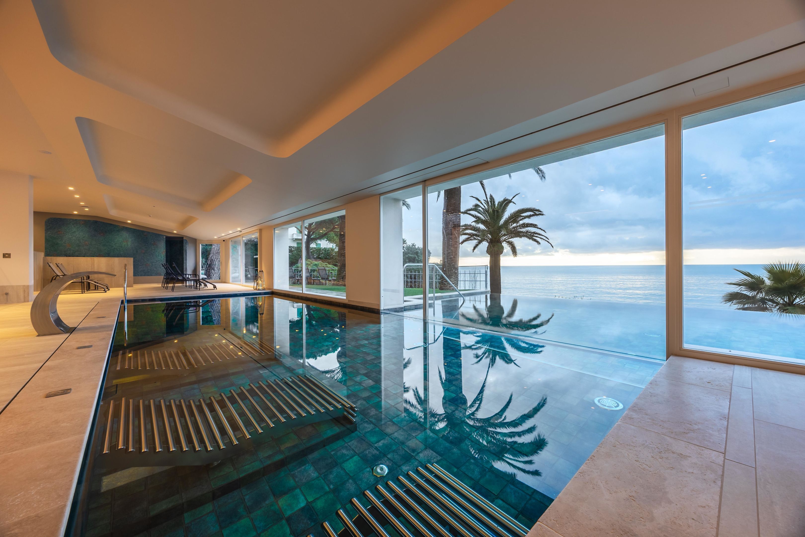 Une piscine intérieure moderne avec des murs en verre et une vue sur l’océan.