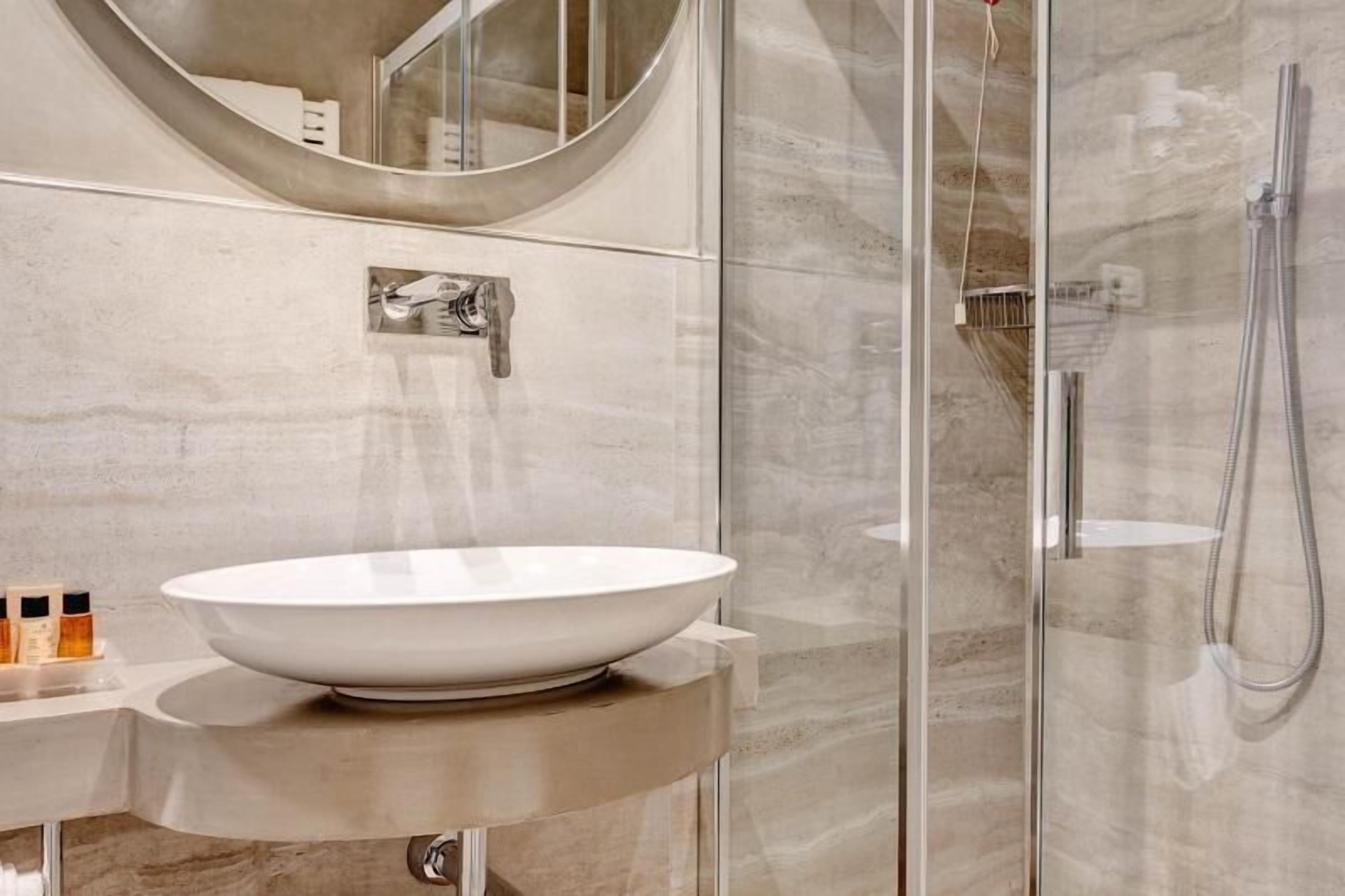 Un baño moderno con un lavamanos blanco de diseño, cabina de ducha con mampara de vidrio y un espejo sobre el lavamanos.