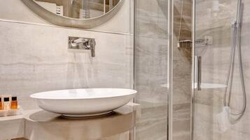 Un baño moderno con un lavamanos blanco de diseño, cabina de ducha con mampara de vidrio y un espejo sobre el lavamanos.