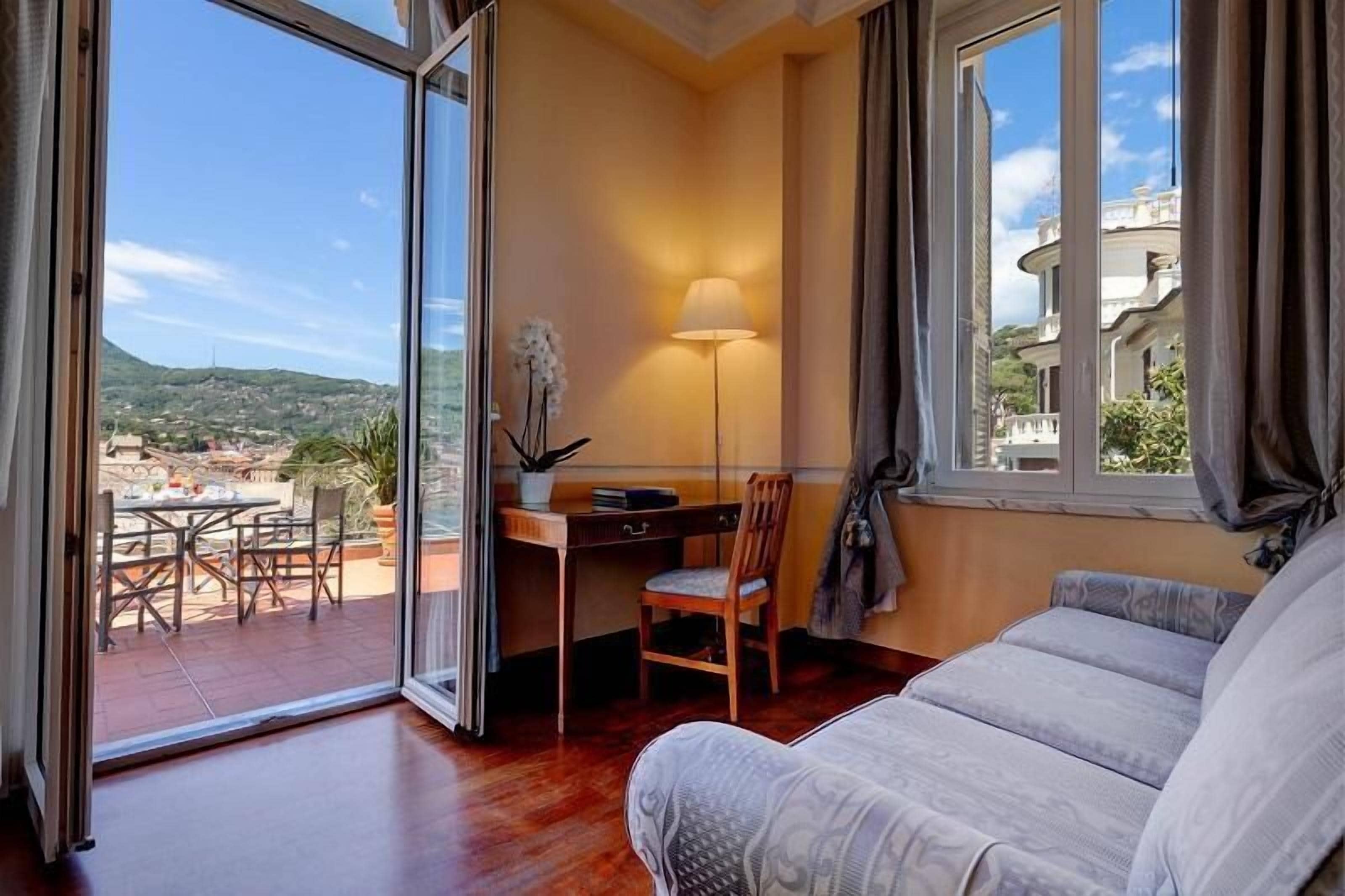 Una habitación con vistas a un paisaje urbano, un escritorio con una lámpara, una silla y un sofá.