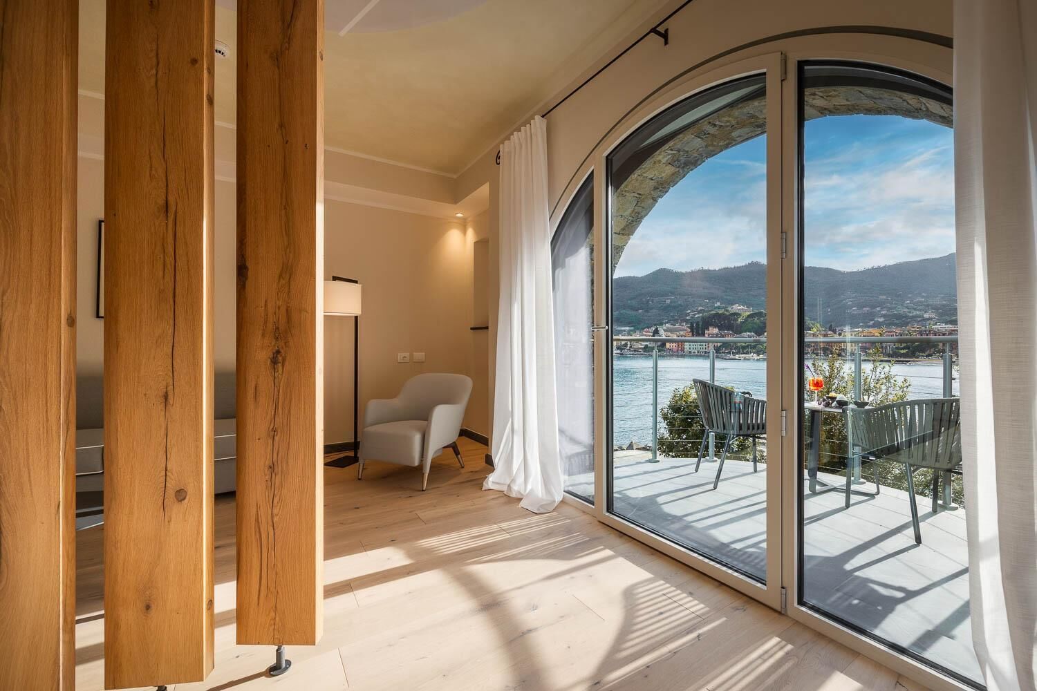 Una habitación con un amplio ventanal corredera que da a un balcón con vistas panorámicas al agua y a las montañas.
