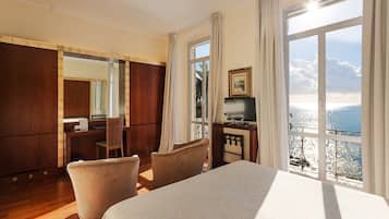 A hotel room with a large bed, a desk with a chair, a television, and a view of the sea.