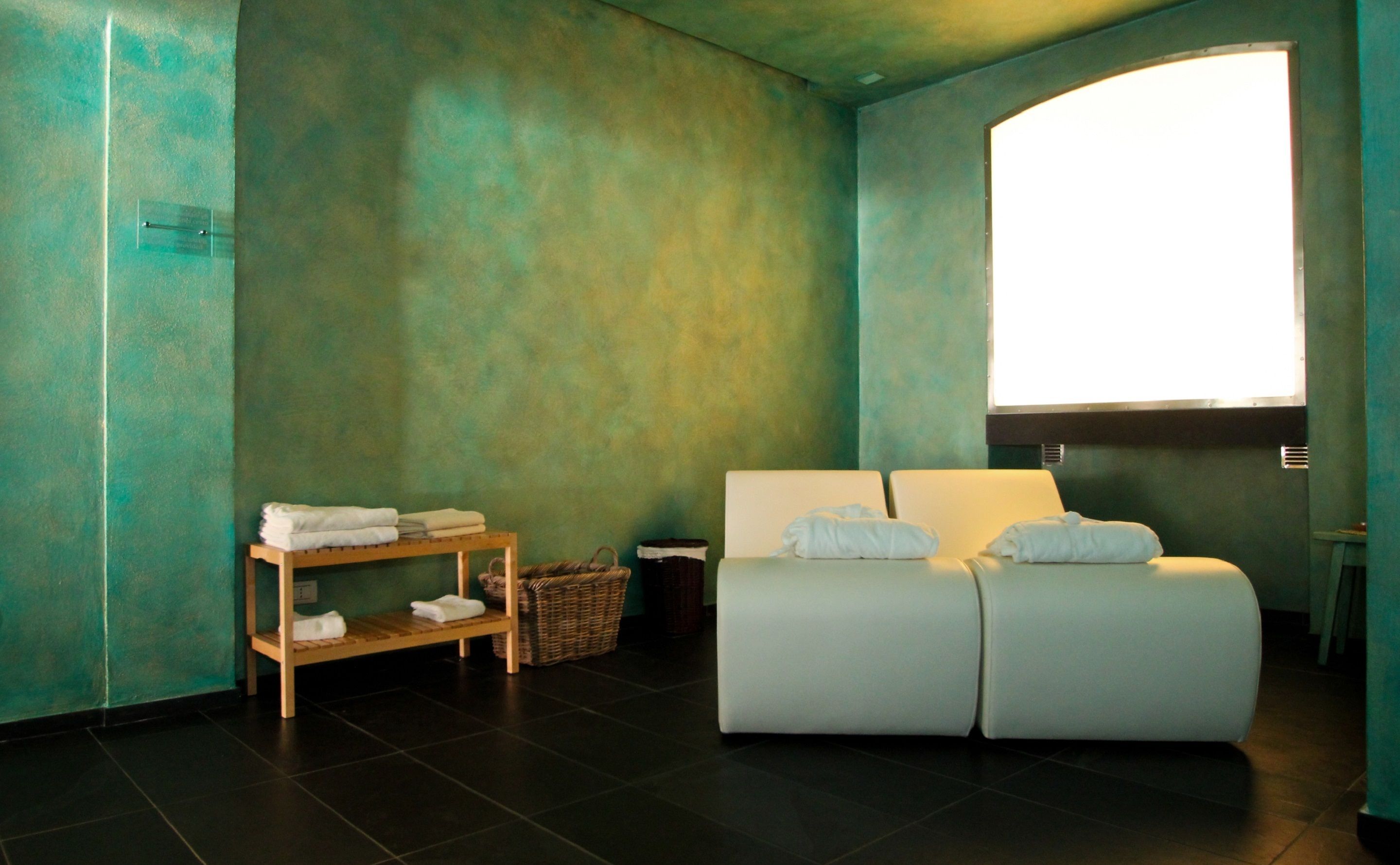 Un cuarto de spa con un ventanal grande, un sofá blanco y un estante de madera con toallas.