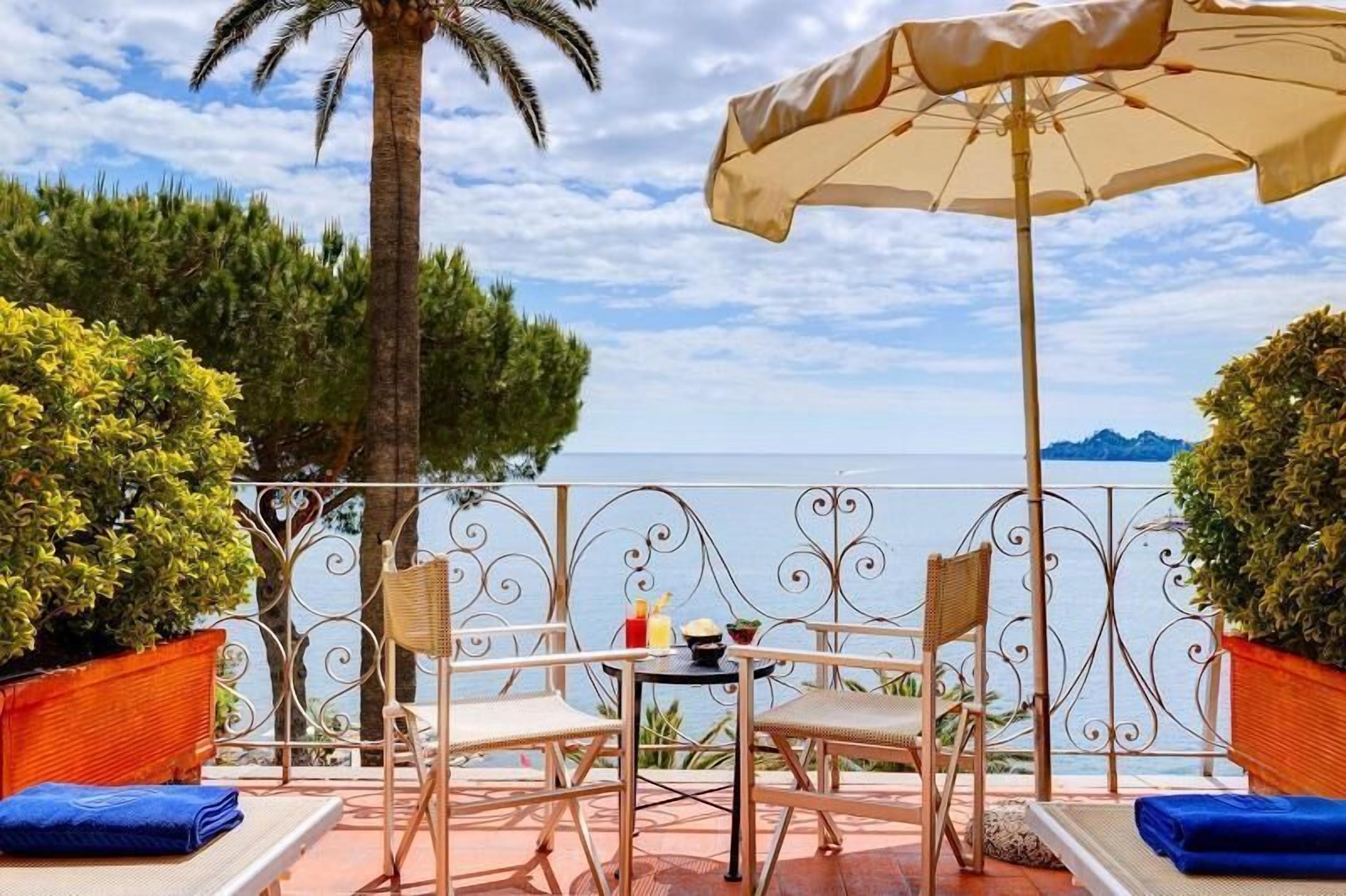 A terrace with a table, chairs, and an umbrella overlooking a body of water.