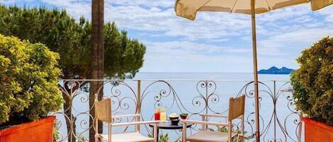 A terrace with a table, chairs, and an umbrella overlooking a body of water.