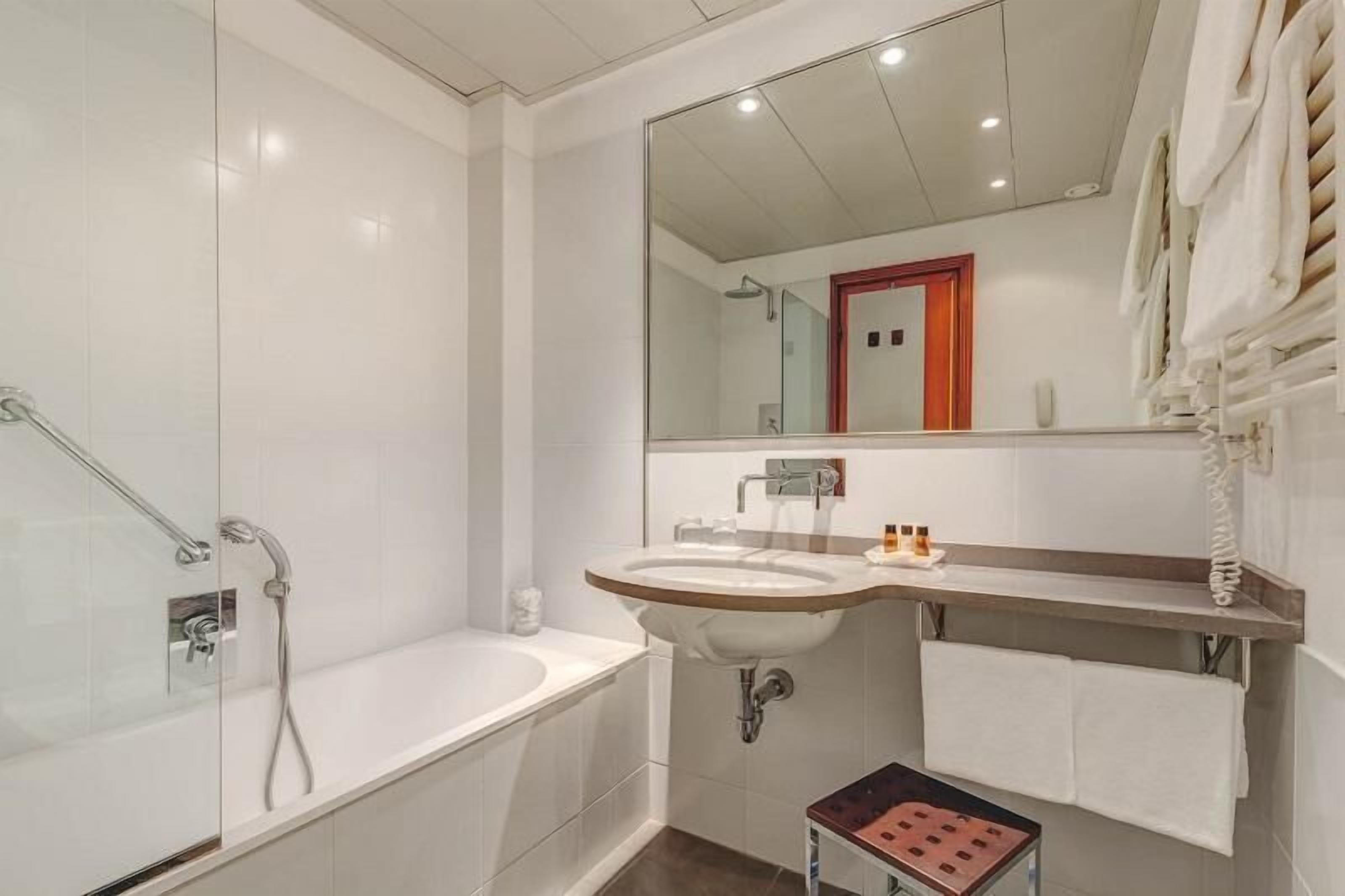 A modern bathroom with a glass-enclosed shower, a sink with a mirror above it, and a towel rack with towels.