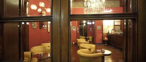 A room with a large mirror reflecting a bar area with leather chairs and a chandelier.