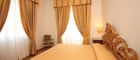A hotel room with a large bed, curtains, a chair, and a nightstand with a lamp.