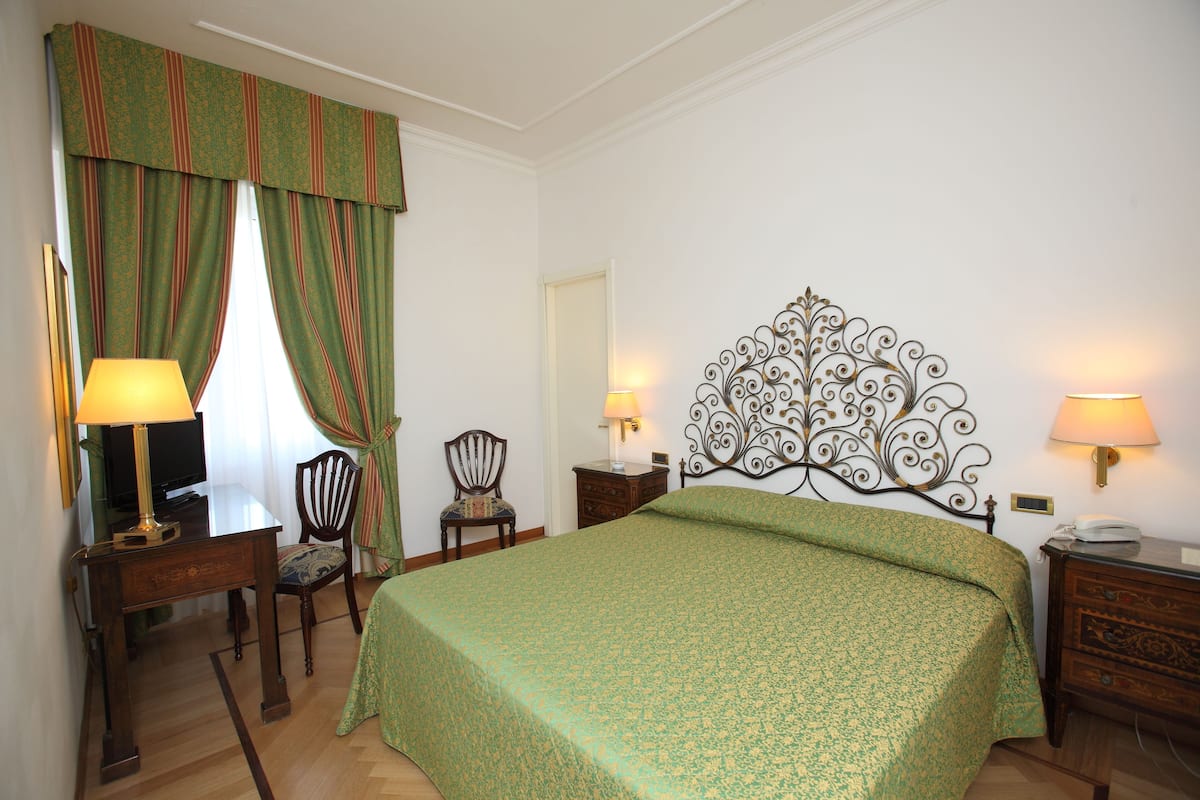 Une chambre d’hôtel avec un grand lit, deux tables de chevet avec des lampes, une chaise, un bureau avec une lampe et un téléviseur.