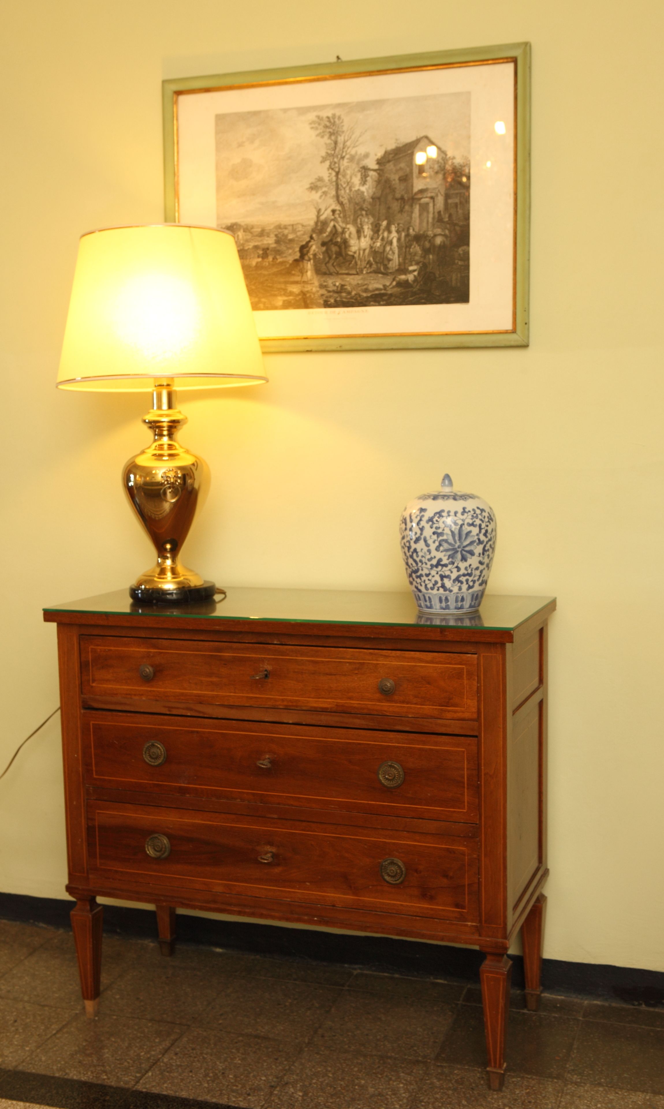 Une commode en bois, sur laquelle sont posés une lampe et un vase.
