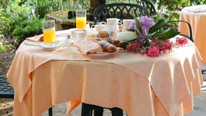 Une table à manger en plein air, agrémentée d’une statue, d’une fontaine et de fleurs roses.