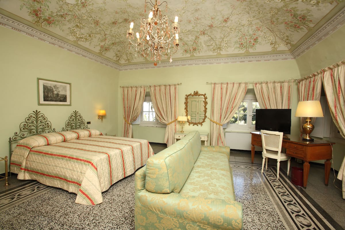 Une chambre d’hôtel avec un lit, un canapé, un bureau, une télévision et un lustre.