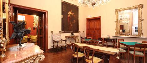 A formal dining room with a long table, chairs, a chandelier, and a large painting on the wall.