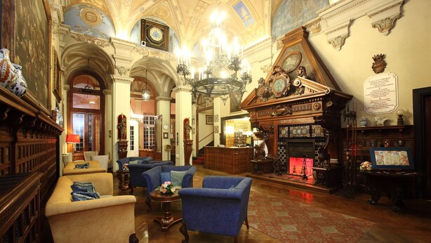 Un vaste hall d’entrée agrémenté de lustres somptueux, d’une cheminée et de meubles classiques.