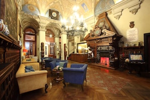 Un vestíbulo imponente con candelabros ornamentados, una chimenea y mobiliario clásico.