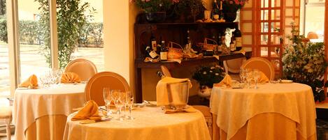 Comedor con mesas redondas cubiertas con manteles amarillos, cada una con copas de vino, platos y cubiertos.