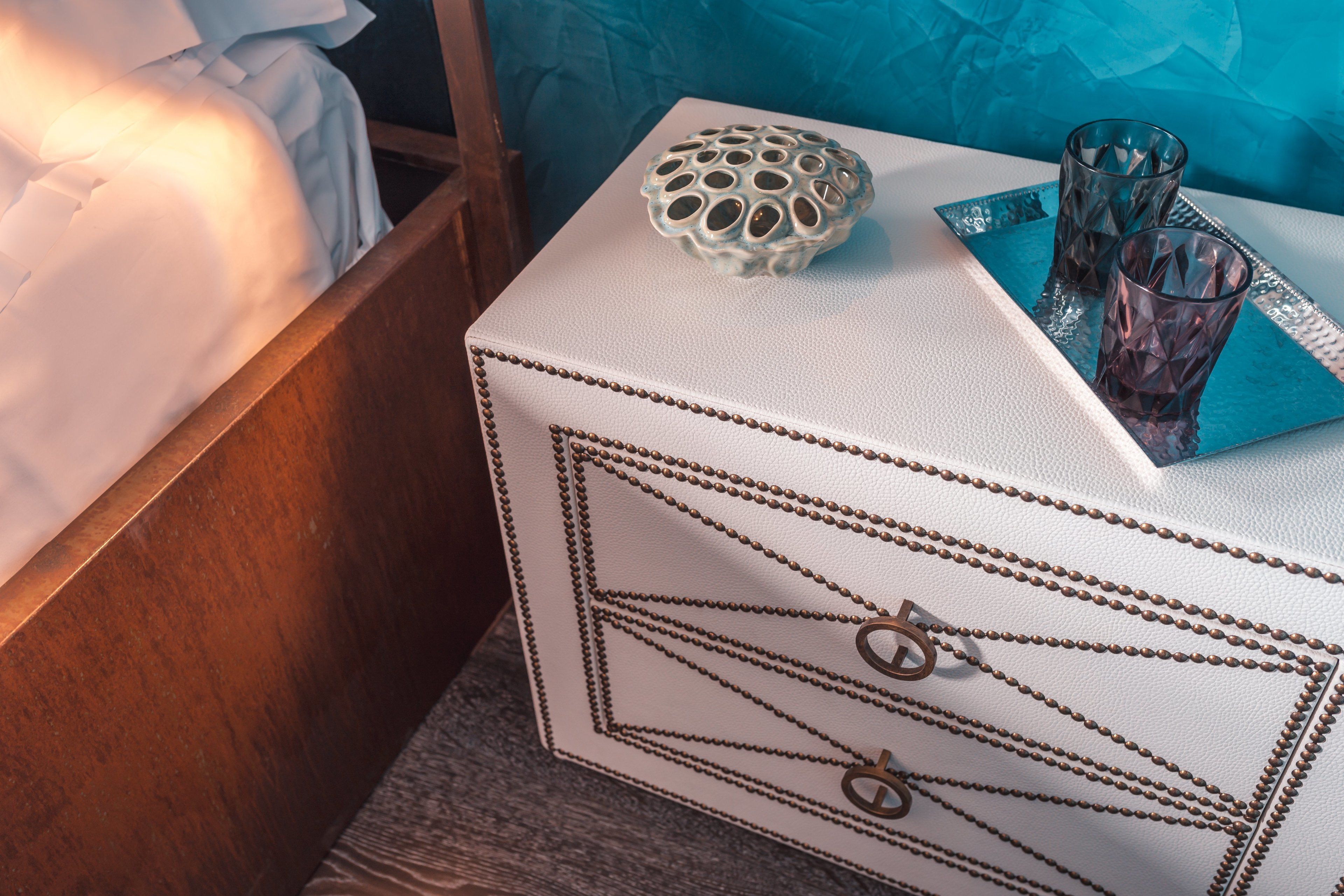 Een witte ladekast met messing handgrepen, een decoratieve glazen schaal en twee glaasjes op een blauwe schaal.