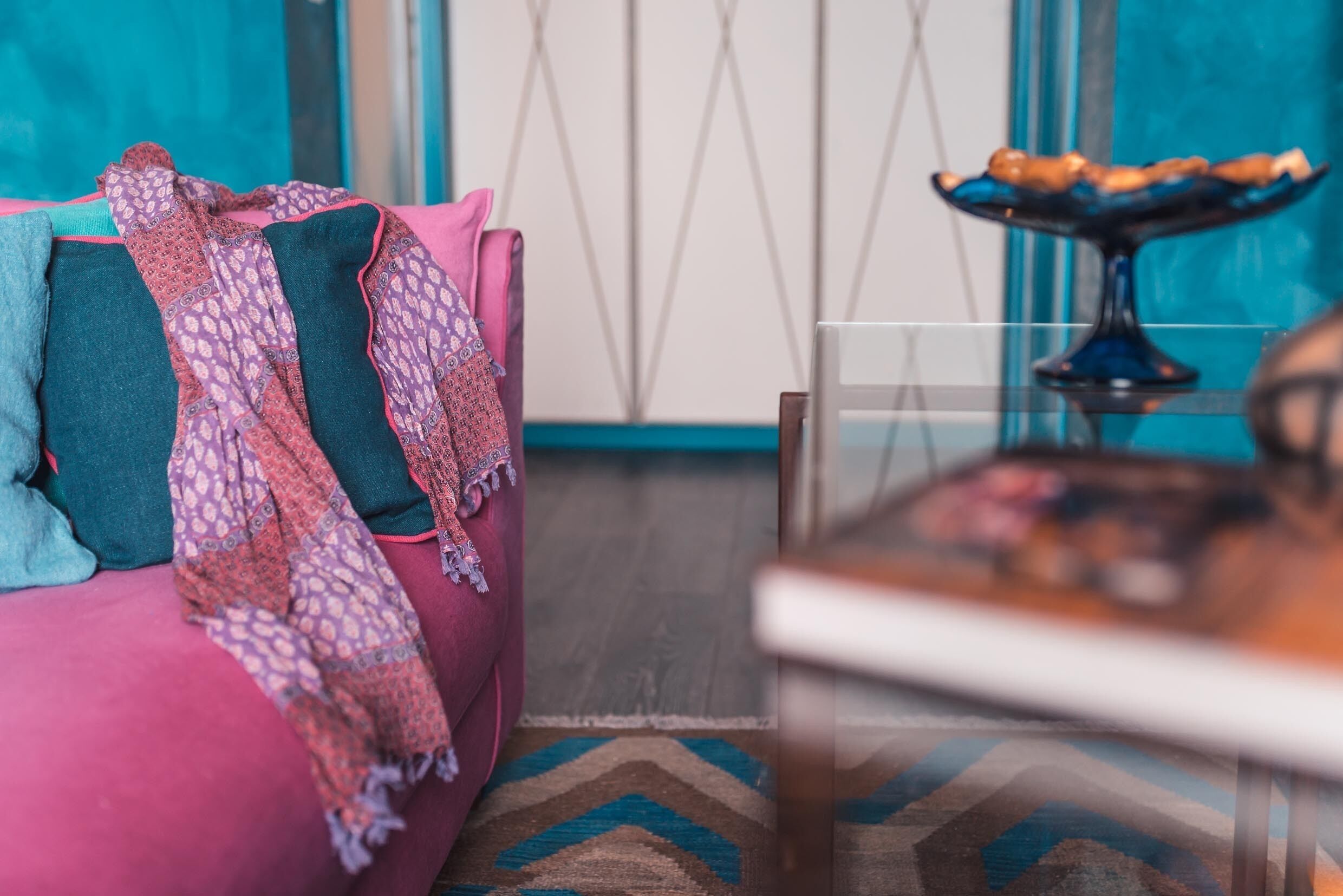 Een gezellige kamer met een roze bank, een decoratief plaid en een vloerkleed met blauwe en bruine patronen.