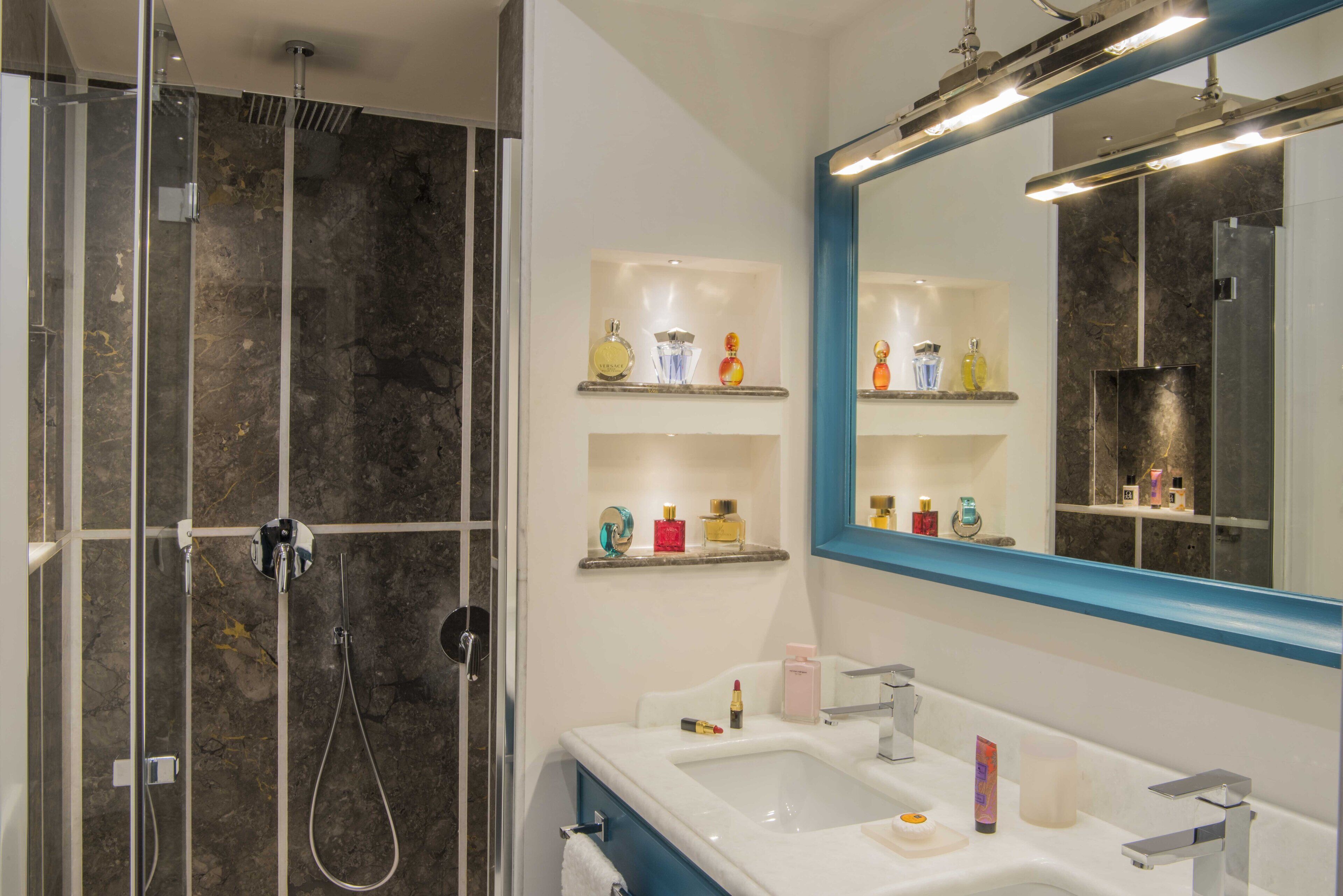 A modern bathroom with a glass-enclosed shower, a white sink with a blue countertop, and shelves with various toiletries.