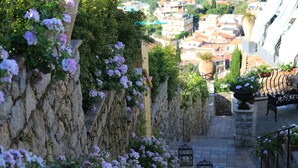 A narrow stone pathway with flower boxes and benches, leading to a town with buildings in the background. - Hotel Villa Ducale (Taormina)