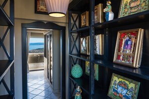 A hallway with a view of the sea, a black shelving unit with framed artwork, and a green decorative object.