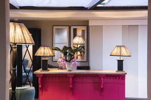 A reception desk with three lamps, a vase with flowers, and a chair.