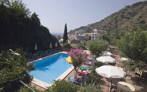 A swimming pool surrounded by lounge chairs and umbrellas, with a mountainous backdrop. - Hotel Villa Sirina (Taormina)